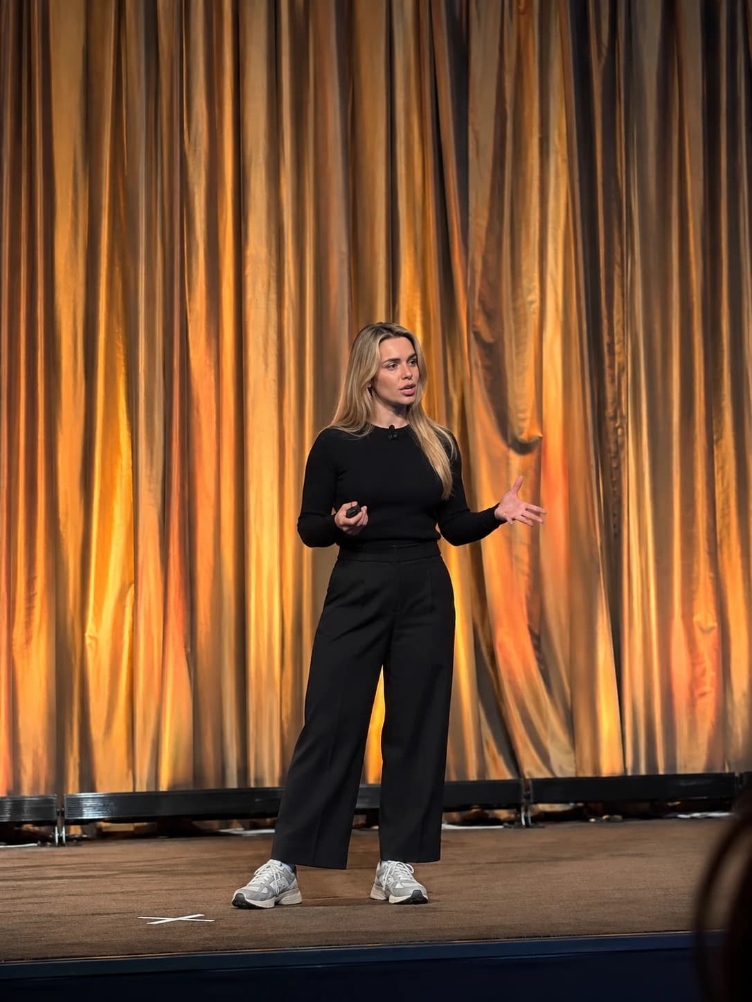 Iryna presenting in front of an amber stage curtain, holding a slide clicker